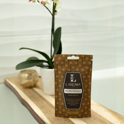 A packet of Dream Haven Bath Salts (CBD Isolates) rests on the bathtub edge beside a potted orchid and gold decor, with white tiled walls in the background.