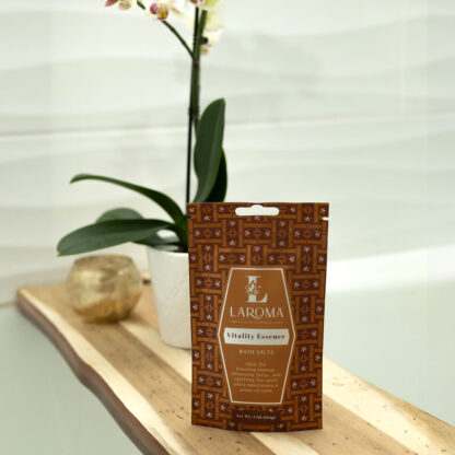 A packet of Dream Haven Bath Salts (CBD Isolates) rests on a wooden bath tray next to a potted plant and white orchid, with a bathtub and tiled wall in the background.