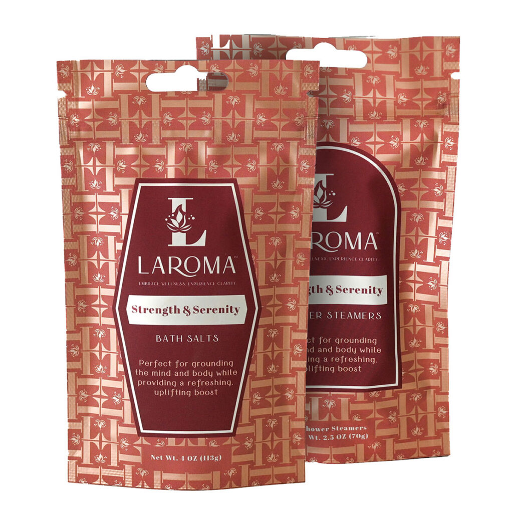 Two red patterned pouches of LAROMA products, one labeled Strength & Serenity Bath Salts and the other Shower Steamers, are standing upright, partially overlapping, with white text and logo on each package.